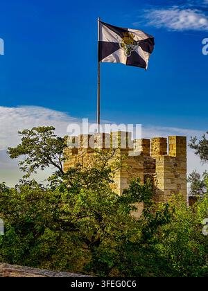 Flagge, die über dem Castelo de São Jorge in Lissabon weht. Eine Flagge weht über den zinnenbekrönten Steinmauern und Türmen der historischen Festung auf dem Hügel. Stockfoto