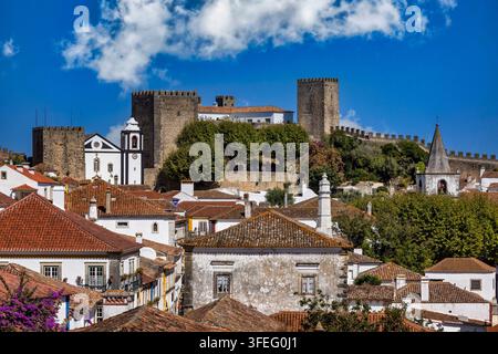 Schloss Óbidos über der mittelalterlichen Stadt in Portugal. Steintürme und befestigte Mauern erheben sich über rotgedeckten Dächern und weiß getünchten Häusern. Stockfoto