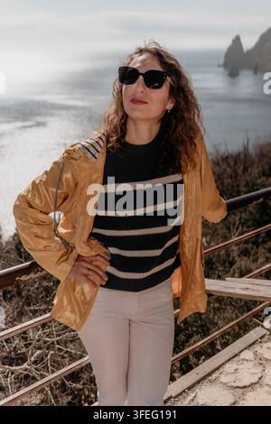 Frau Küstenabenteuer junge Frau in gelber Jacke steht an einem Küstenausblick und genießt die Meeresaussicht an einem sonnigen Tag Stockfoto