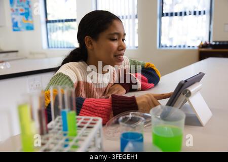 Schulkind in gestreiftem Pullover tippt auf Tablet auf Ständer im Wissenschaftslabor mit Reagenzgläsern Stockfoto