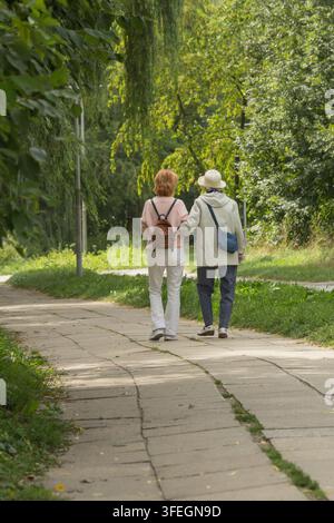 Zwei Frauen gehen gemeinsam einen von Bäumen gesäumten Parkweg an einem sonnigen Tag entlang Stockfoto