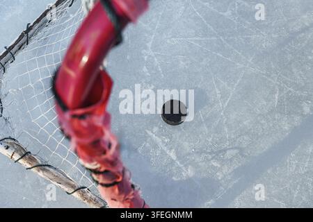 Ein Eishockeypuck im Tor, auf strukturiertem Eis mit Schlittenspuren. Stockfoto