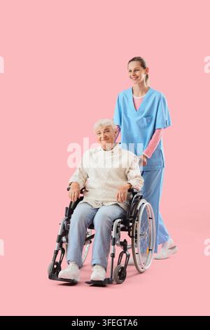 Altenpflege und betreutes Wohnen, Krankenschwester schiebt eine ältere Frau im Rollstuhl für medizinische Unterstützung und Patientenrehabilitation auf einem festen rosa Hintergrund Stockfoto