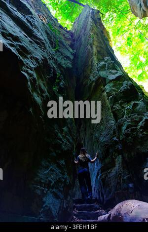 Eine Frau von hinten gesehen, die auf Steinstufen zwischen zwei riesigen Felsen geht, stimmungsvoller Pfad, niedrige Perspektive Stockfoto