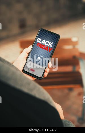 Black-Friday-Verkaufsaktion auf dem Smartphone-Bildschirm. Frau hält ein Telefon und zeigt die Black-Friday-Verkaufsaktion an. Stockfoto