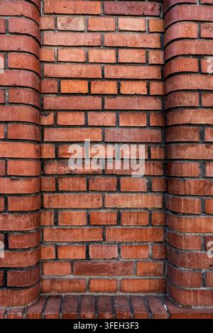 Nahaufnahme einer roten Ziegelmauer mit gebogenen Seitenstützen, die eine vertiefte Nische bilden, reich an warmer Mauertextur und wiederholtem Muster Stockfoto