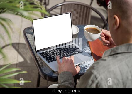 Reifer Mann arbeitet an einem Laptop, während er in einem Außencafé Kaffee trinkt. Fernarbeit, Freelancing, flexibler Arbeitsplatz und Digital-Nomaden-Lebensstil. Stockfoto