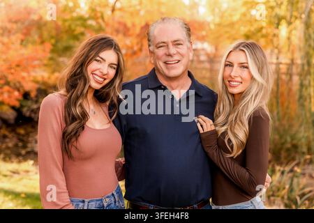Zufriedener Vater posiert mit seinen beiden erwachsenen Töchtern im Freien im Herbst Stockfoto