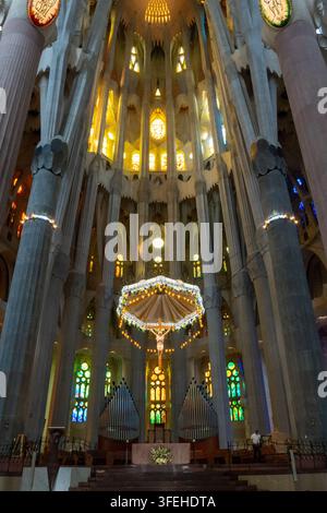 Barcelona, Spanien 01.09.2026 Religiöse Innenräume zeigen Kruzifix, Altar und Orgelpfeifen unter hohen Rippengewölben. Farbglas und warme Lampen erhellen Stockfoto