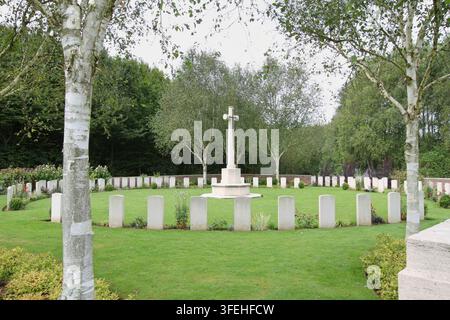 Das weiße steinerne Kreuz der Opferung steht zwischen Reihen von Grabsteinen hinter einer niedrigen Backsteinmauer auf einem Commonwealth-Militärfriedhof in Belgien. Stockfoto