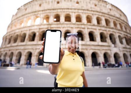 Weiblicher Tourist zeigt Smartphone mit leerem Bildschirm vor dem Kolosseum in Rom. Stockfoto