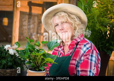 Ein Seitenansicht-Kopf-und-Schultern-Porträt einer mittelalten Frau im Freien, die einen Strohhut trägt und warm in die Kamera lächelt. Stockfoto