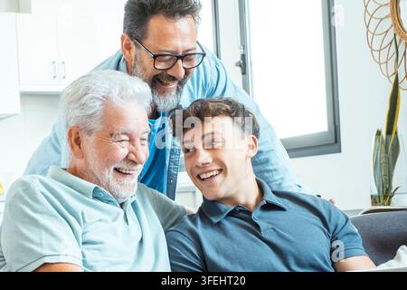 Großvater, Vater und jugendlicher Enkel lachen zusammen auf einem Sofa, genießen warme familiäre Bindungen und multigenerationale Verbindung in einem hellen modernen Ho Stockfoto