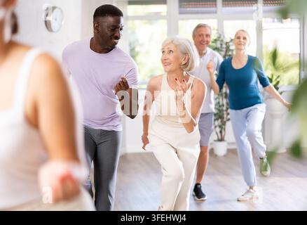 Mittealter Afrikanisch-Amerikaner lernt Latein-Salsa-Tanz mit älterer Dame. Tanzstudio-reife Kunden bewegen sich im Hintergrund Stockfoto