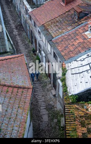 Porto, Portugal - 2024.03.16. 17:05: Eine vertikale, hochwinklige Perspektive aus der Vogelperspektive fängt eine gewundene, historische Kopfsteinpflastergasse ein, die tief eingebettet ist Stockfoto