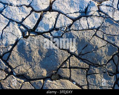 Rissige trockene Erde, die eine abstrakte Textur und Muster bildet, symbolisiert Dürre und Umweltprobleme wie den Klimawandel Stockfoto