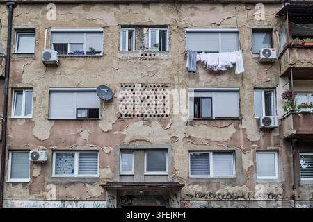 Verwittertes Wohngebäude mit abblätterndem Putz, Rolltoren, Klimaanlagen und Wäsche, die an den Fenstern in Tuzla, Bosnien, hängt Stockfoto