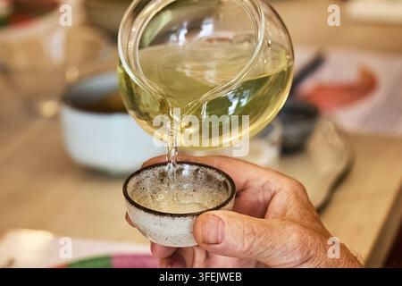 Hand gießt grünen Tee aus einer Glasteekanne in eine Tasse Stockfoto