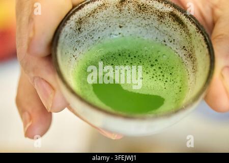 Hände, die eine traditionelle Keramiktasse mit Matcha-Tee halten Stockfoto