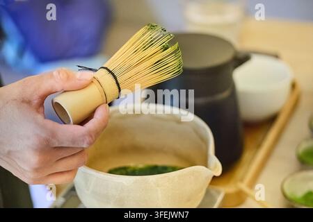 Hand hält ein Chasen und schaumt Matcha-Grüntee in einer Schüssel auf Stockfoto