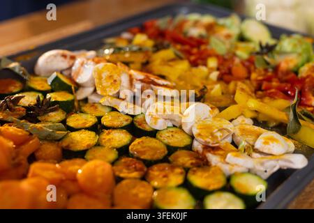 Geröstetes Gemüse glitzert auf dem Backblech in der Küche und zeigt Zucchini, Pilze, Paprika Stockfoto