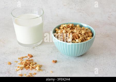 Müsliriegel in einer blauen Schüssel mit Milch in einem Glas zum Frühstück auf einer weißen Oberfläche Stockfoto