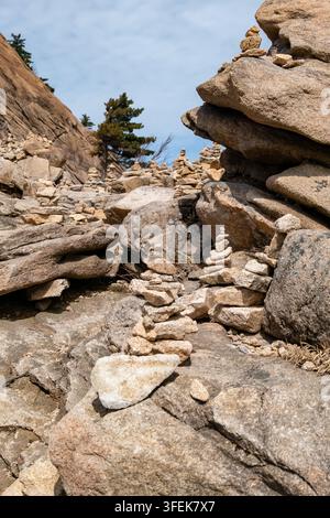 Felsiger Bergpfad mit gestapelten Steinhaufen zwischen großen Granitblöcken, eingerahmt von Kiefern und einem klaren blauen Himmel. Stockfoto