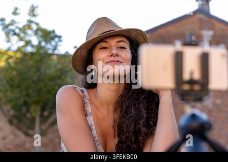 Junge Frau mit Fedora-Hut, die sich mit einem Smartphone für einen Vlog filmt Stockfoto