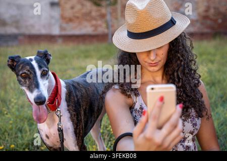 Frau mit Strohhut, die im Freien ein Selfie mit ihrem Windhund macht Stockfoto