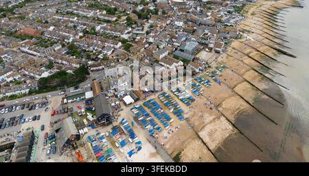 Touristen entspannen sich am Kieselstrand von Whitstable neben traditionellen Schindelhäusern und genießen die vertäuten Boote entlang der Küste von Kent. Stockfoto