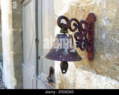 Antike Eisen Glocke neben einer Holztür an einer Steinmauer, Gers, Montesquiou, Frankreich Stockfoto