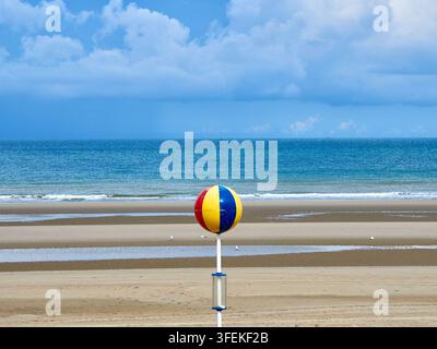 Farbenfroher Strandballmarker am sandigen Strand mit ruhigem Ozean und bewölktem Himmel Stockfoto