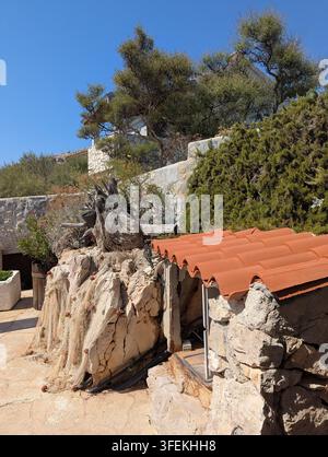 Pirovac, Kroatien, 16. August 2026 Rustikes Hügelhaus aus Stein und Putz, eingerahmt von dichten immergrünen Bäumen, Terrakotta-Dachziegel, trockener Garten Stockfoto