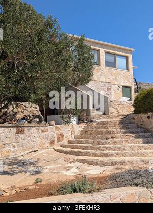 Pirovac, Kroatien, 16. August 2026 Steines Wohnhaus mit Außentreppe, verwitterten Felswänden, dichtem grünen Baumbewuchs und hellem blauem Himmel, aufgenommen Stockfoto