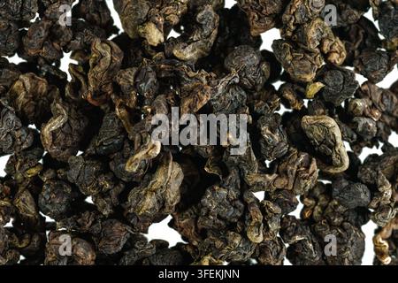 Makroaufnahme von trockenen GABA-Smaragd-Oolong-Teeblättern, die eine eng gerollte Blatttextur und natürliche dunkelgrüne und braune Töne zeigen. Ideal für Tee und Bev Stockfoto