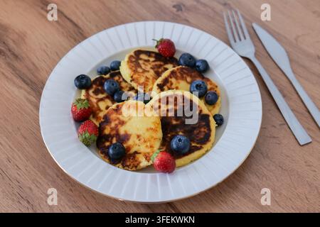 Ein Teller mit Pfannkuchen und Blaubeeren steht links auf einem hellen Holztisch neben einer silbernen Gabel und einem Messer. Minimale Frühstücksgestaltung Stockfoto