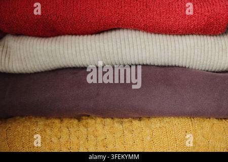 Nahaufnahme von farbenfrohen gestrickten Pullovern, die aufeinandergestapelt sind, mit Betonung auf weichen Texturflächen, warmer Kleidung und saisonaler Herbst-Winter-Mode. Stockfoto