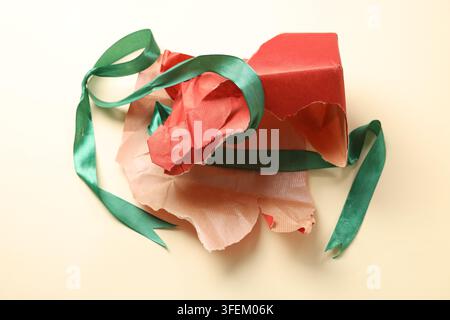 Zerknittertes zerrissenes Geschenkpapier und Band auf beigem Hintergrund, Nahaufnahme Stockfoto