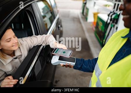 Frau, die für Gas bezahlt, indem sie kontaktlos per Smartphone bezahlt Stockfoto