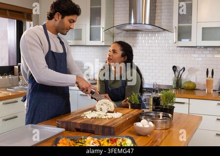 Afroamerikanisches Paar trägt Schürzen und schneidet Blumenkohl in der Küche mit einem Küchenmesser und Brötchen-Gemüse Stockfoto