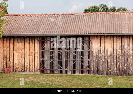 Symmetrisch gerahmte verwitterte Holzscheune mit großen lamellierten Doppeltüren und Wellblechdach in einer ländlichen Umgebung. Landwirtschaftskonzept. Stockfoto
