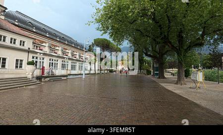 MERANO, ITALIEN, 12. AUGUST 2026: Nahaufnahme des großen Metallschilds „Merano“ im historischen Zentrum der Kurstadt, umgeben von Blumenbeet Stockfoto