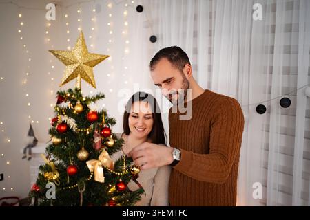 Fröhliches Paar dekoriert zusammen den Weihnachtsbaum für die Winterfeiertage Stockfoto