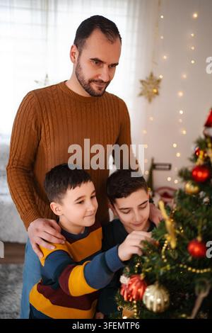 Vater und Söhne schmücken gemeinsam zu Hause den Weihnachtsbaum Stockfoto