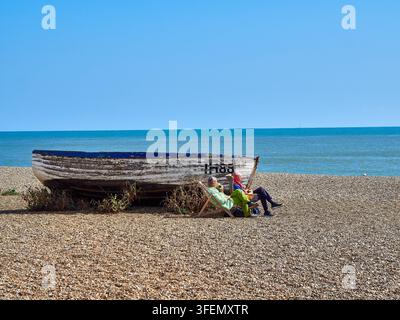 Älteres Paar entspannt in Liegestühlen neben einem alten Fischerboot am Kieselstrand Stockfoto
