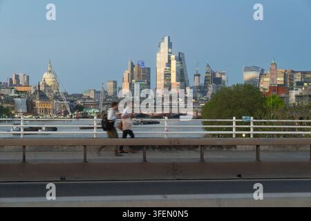 Pendler gehen bei Dämmerung über die Waterloo Bridge, vorbei an der Themse, der St. Paul's Cathedral und der Skyline der City of London. Stockfoto