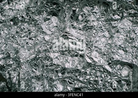 Silberne zerknitterte Aluminiumfolie, flache Hintergrundstruktur. Glänzende Metallsilbergraue Folie zerknitterte Textur Hintergrund. Abstrakter Hintergrund der zerknitterten Folie Stockfoto