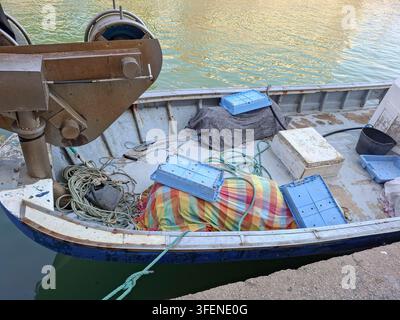 Ein kleines gewerbliches Fischerboot liegt im Hafen vor Anker. Seile und Ausrüstung sind auf dem Deck angeordnet. Plastikboxen sind gestapelt und bereit für den Einsatz. Stockfoto