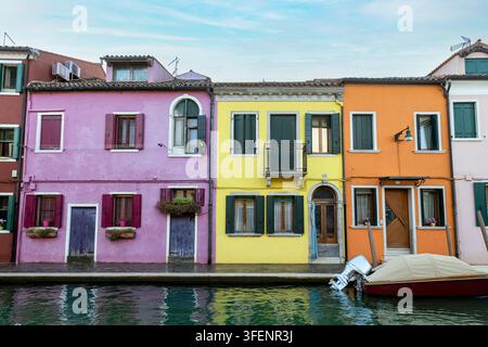 Farbenfrohe rosa, gelbe und orangefarbene Hausfassaden säumen einen Kanal mit einem vertäuten Boot, Burano, Venedig, Italien Stockfoto