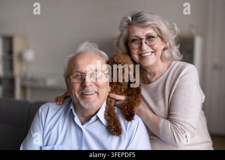 Porträt eines glücklichen Seniorenehepaars und eines süßen Pudels drinnen Stockfoto